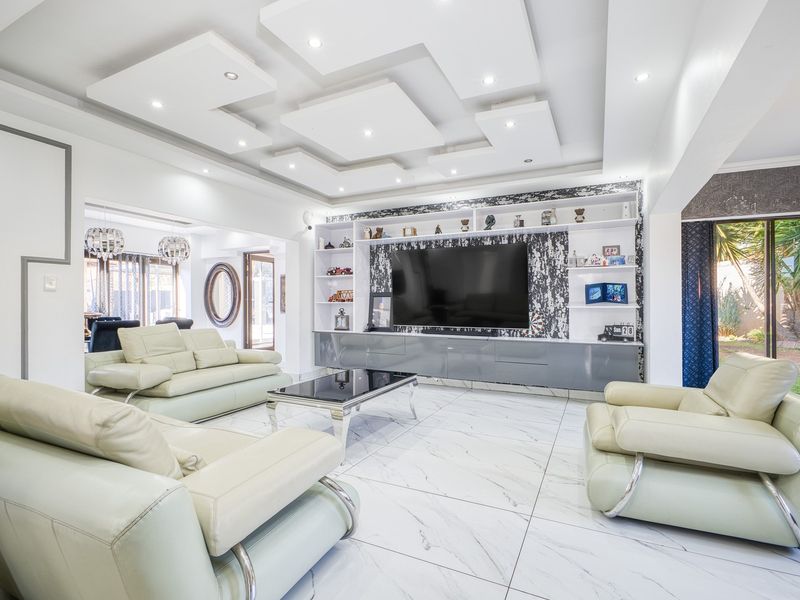 Spacious living room featuring a modern recessed ceiling with downlights, marble-look floor tiles, and a large built-in media wall unit.