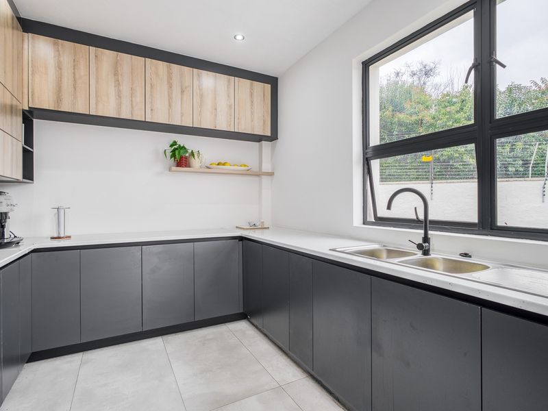 Modern kitchen featuring sleek dark grey lower cabinetry, light wood-tone upper cabinets, stone countertops, and a double sink with a contemporary black mixer tap.