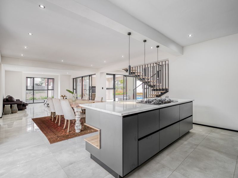 Modern open-plan living area featuring a sleek kitchen island with gas cooktop, recessed lighting, and a contemporary staircase, flowing seamlessly to outdoor spaces.