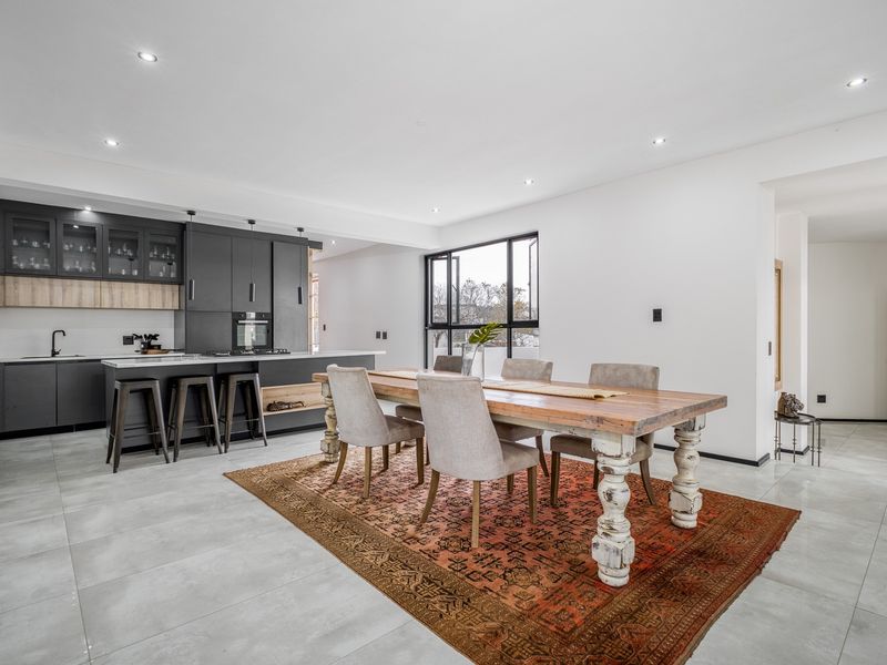 Modern open-plan kitchen and dining area featuring sleek dark cabinetry, a central island, and large windows providing ample natural light.