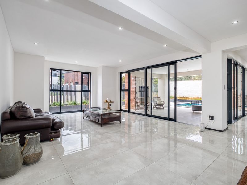 Spacious open-plan living area featuring large format porcelain tiles, recessed lighting, and expansive aluminium sliding doors providing seamless access to the outdoor patio and pool.