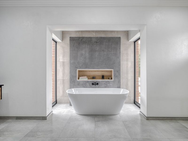 Modern bathroom featuring a sleek freestanding bathtub, a recessed wall niche, and large windows providing natural light.
