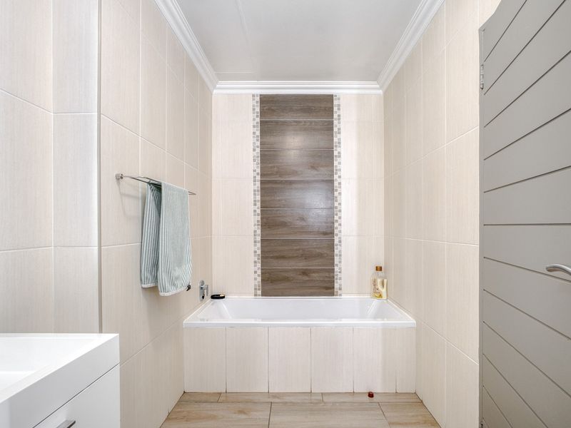 A clean, modern bathroom featuring a built-in bathtub with decorative tile inlay, a vanity basin, and neutral wall tiling.