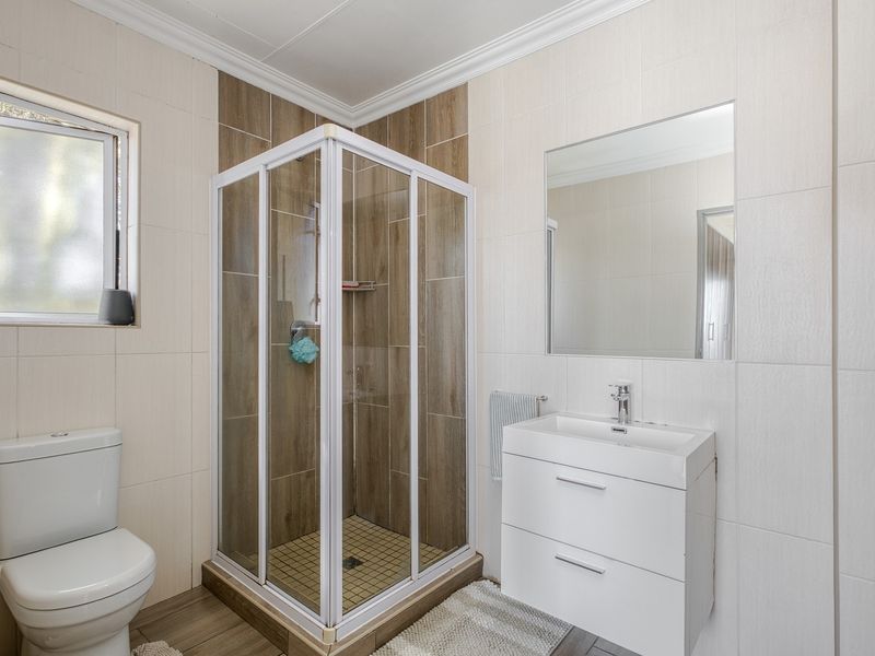 Modern bathroom featuring a corner shower enclosure, wall-mounted vanity with basin, and neutral tiled finishes throughout.