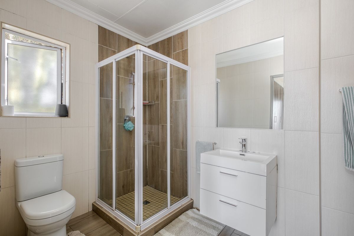 Modern bathroom featuring a corner shower enclosure, wall-mounted vanity with basin, and neutral tiled finishes throughout.