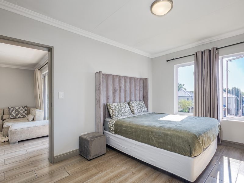 A well-maintained bedroom featuring tiled flooring, neutral wall finishes, and natural light through a window, with an adjoining living area visible.