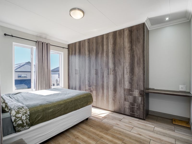 A well-maintained bedroom featuring extensive built-in wooden cabinetry, a matching integrated desk, tiled flooring, and large windows providing natural light.
