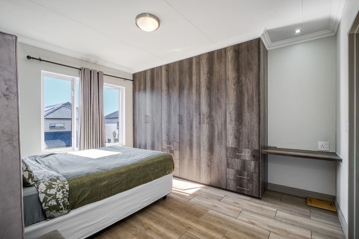 A well-maintained bedroom featuring extensive built-in wooden cabinetry, a matching integrated desk, tiled flooring, and large windows providing natural light.