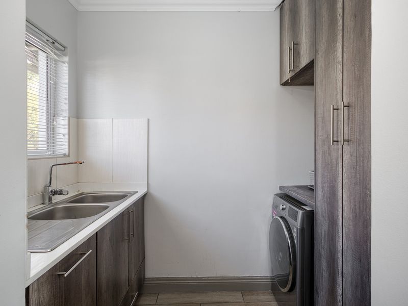 A clean and functional laundry room featuring built-in cabinetry, a double stainless steel sink, and tiled flooring.