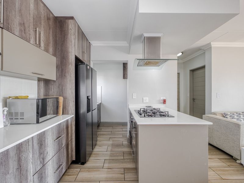 Modern kitchen featuring wood-grain cabinetry, stone countertops, a central island with a gas hob, and high-quality stainless steel extractor fan.