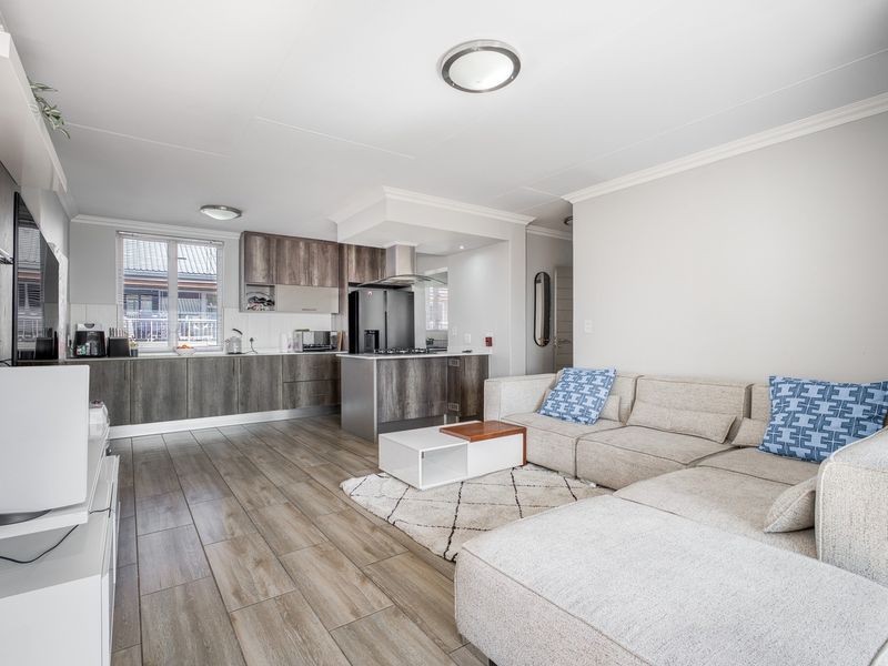 Modern open-plan living area featuring wood-look tile flooring and a contemporary kitchen with built-in cabinetry, island, and integrated appliances.