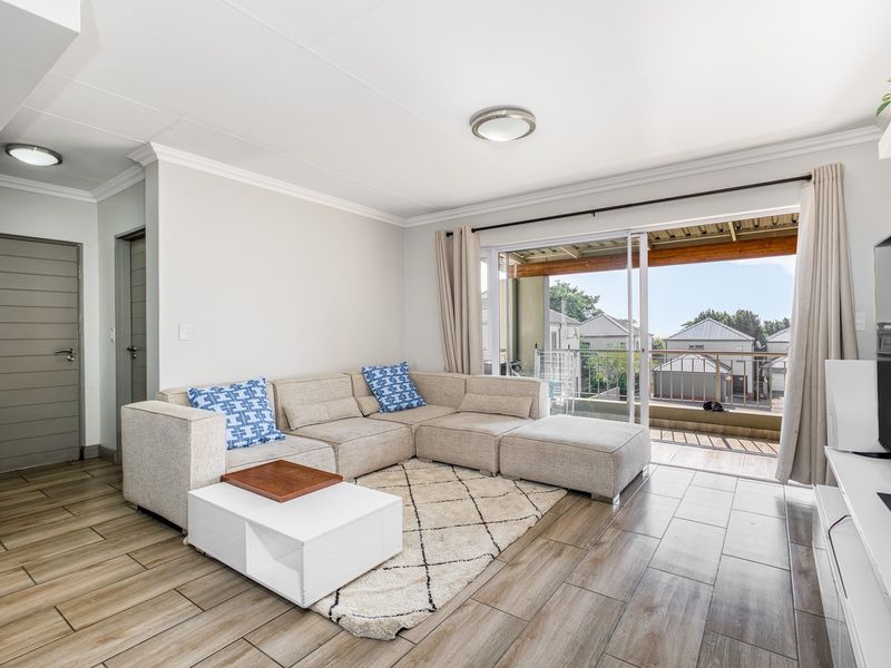 A bright and well-maintained living room featuring wood-look tiled flooring, modern ceiling lighting, and a large sliding door leading to an outdoor balcony.
