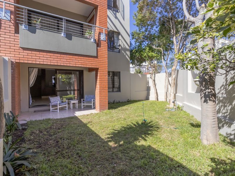 A private rear garden featuring a tiled patio, sliding door access to the interior, and a small lawn area enclosed by boundary walls.