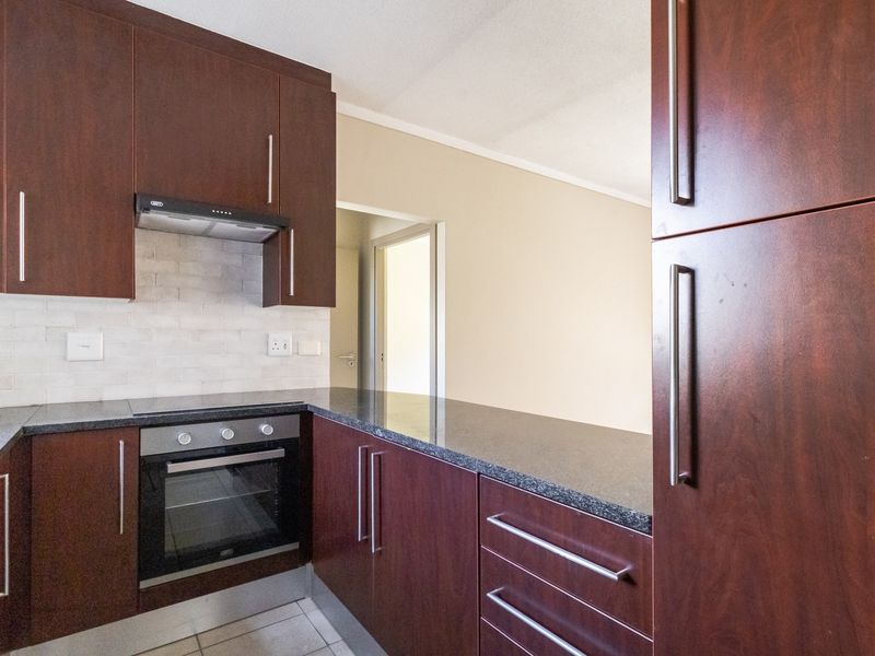 A modern kitchen featuring dark wood cabinetry, granite countertops, a built-in oven, and a stylish subway tile backsplash.