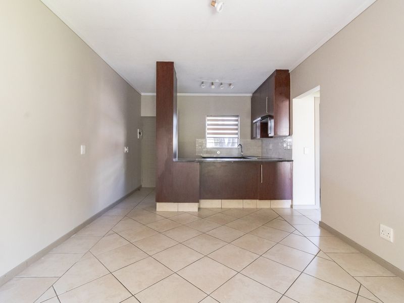 An open-plan living and kitchen area featuring dark wood cabinetry, tiled flooring, and neutral wall tones, offering a functional and versatile layout.