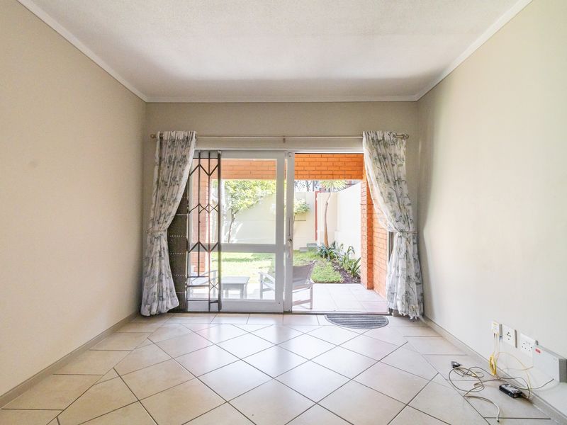 An empty living room featuring tiled flooring and a sliding glass door that provides direct access to a private patio and garden area.