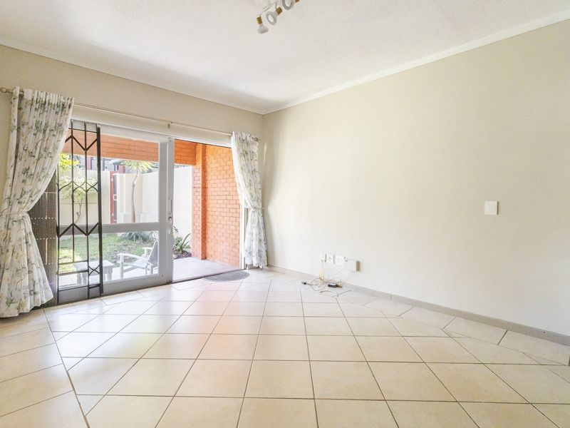 A bright, empty living room featuring neutral tiled flooring and a sliding glass door providing direct access to an outdoor patio area.