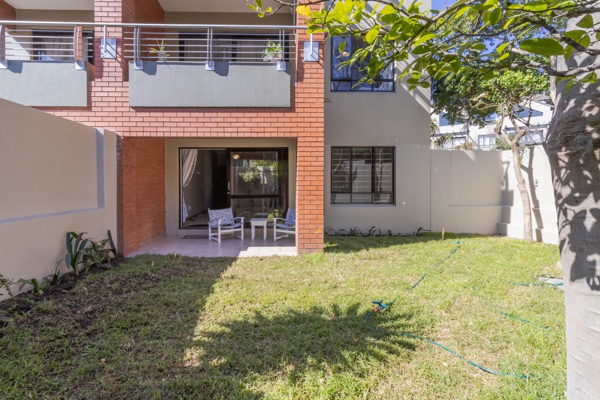 Rear view of the apartment featuring a private garden, a covered tiled patio, and an upper-level balcony with modern metal railings.
