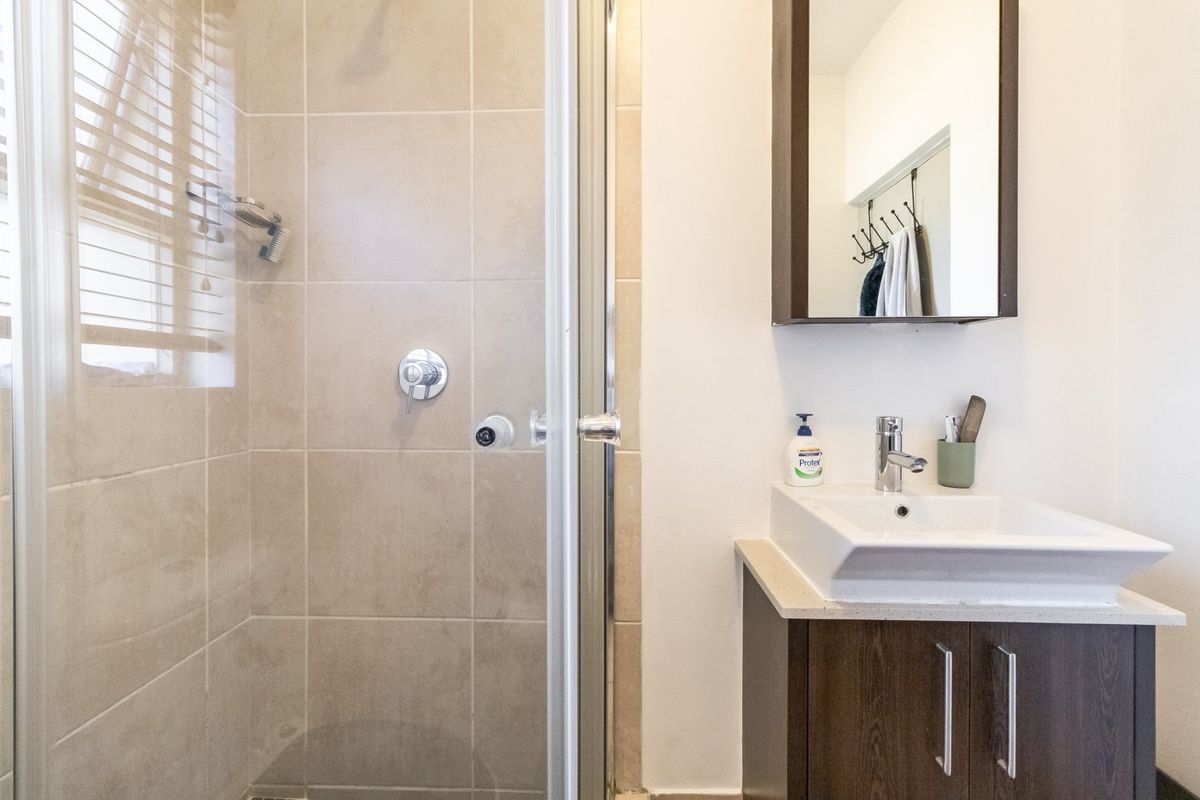 A functional bathroom featuring a glass-enclosed shower with tiled walls, a modern vanity with basin, and a mirrored medicine cabinet.