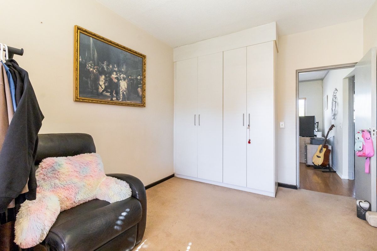 A bedroom featuring neutral walls, carpeted flooring, and a white built-in wardrobe providing ample storage space.