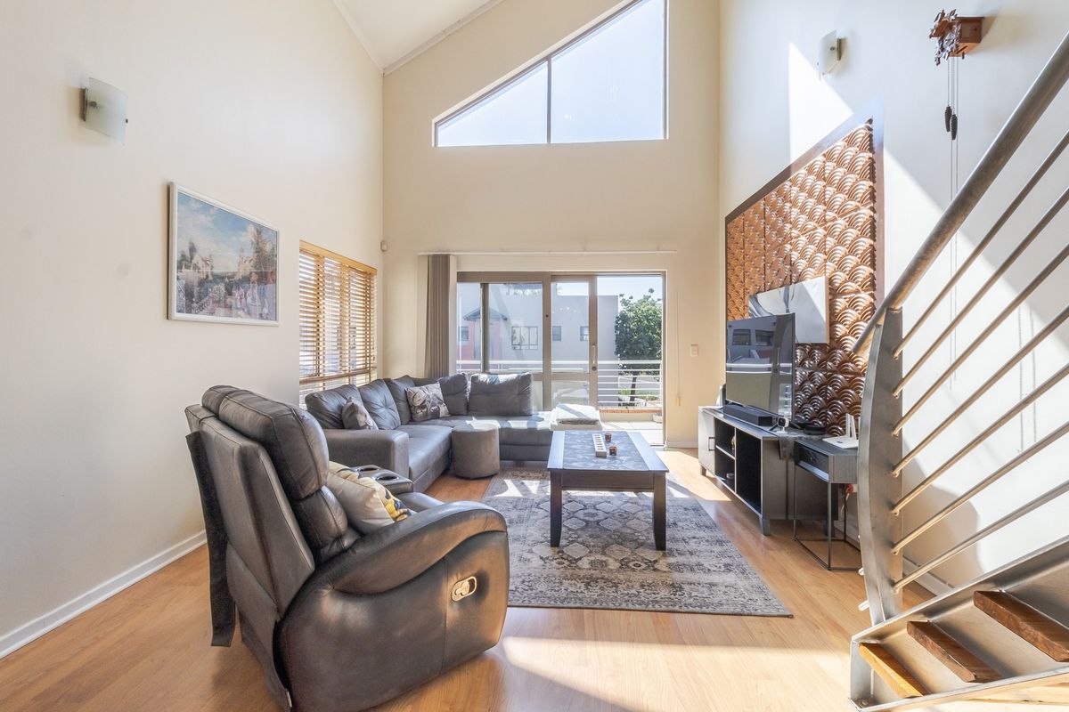 Spacious living room featuring a high vaulted ceiling, large triangular window, and a modern metal staircase, leading out to a balcony.