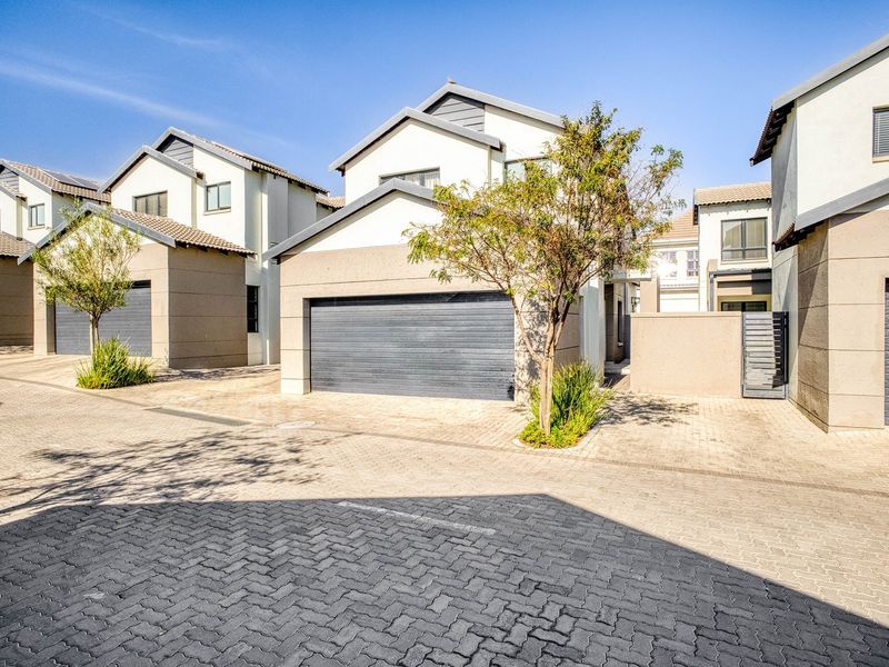 Front view of a modern townhouse complex featuring paved driveways, double garages, and well-maintained plastered facades under a clear blue sky.