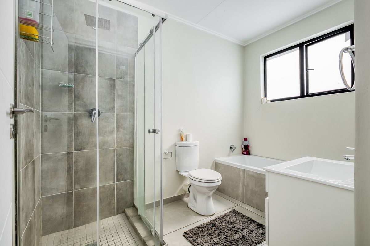 A modern bathroom featuring a glass-enclosed shower, a built-in bathtub, a vanity basin, and a toilet with neutral grey tiling.