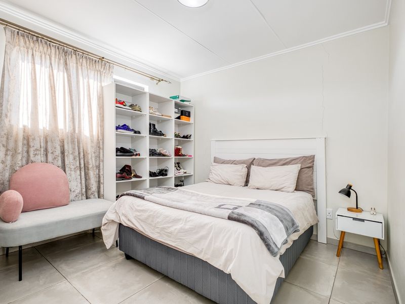 A bedroom featuring tiled flooring and a neutral color palette, currently utilized with a bed and storage shelving.