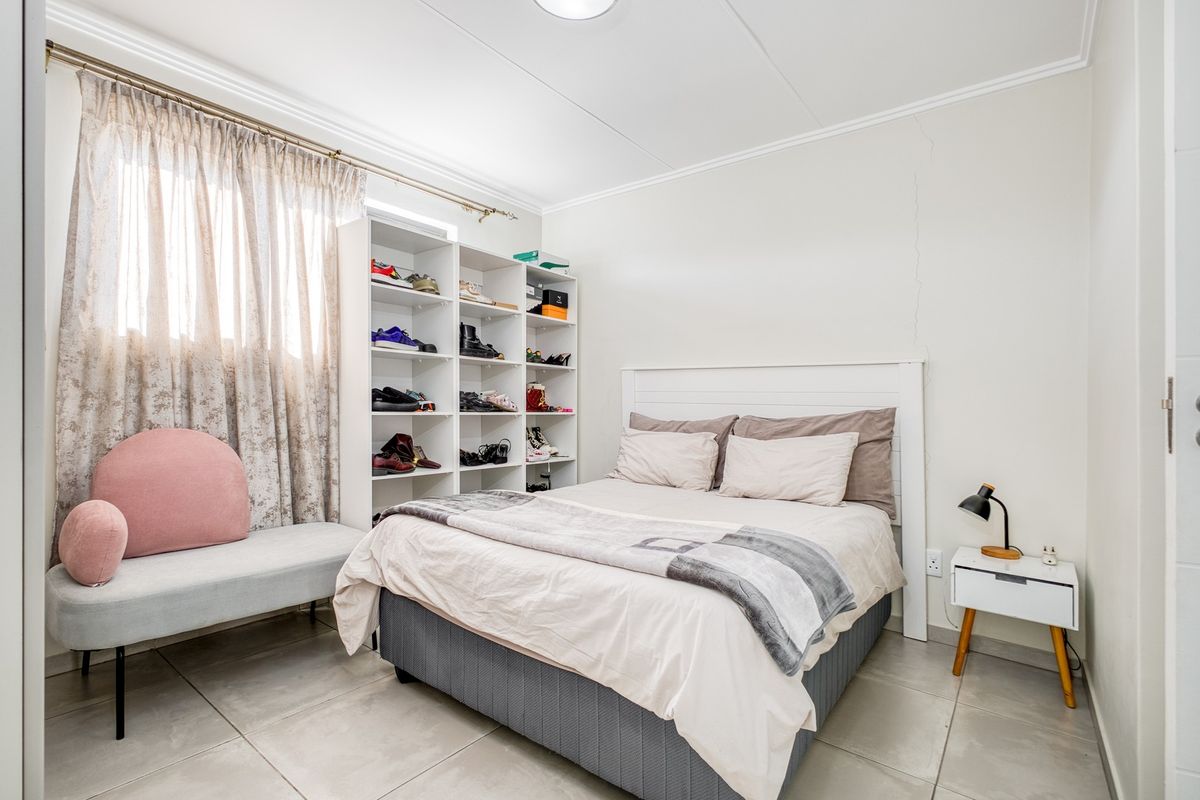 A bedroom featuring tiled flooring and a neutral color palette, currently utilized with a bed and storage shelving.