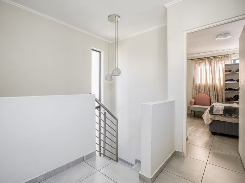 A bright upstairs landing area featuring tiled flooring, a modern metal balustrade staircase, and pendant lighting, leading into an adjacent bedroom.