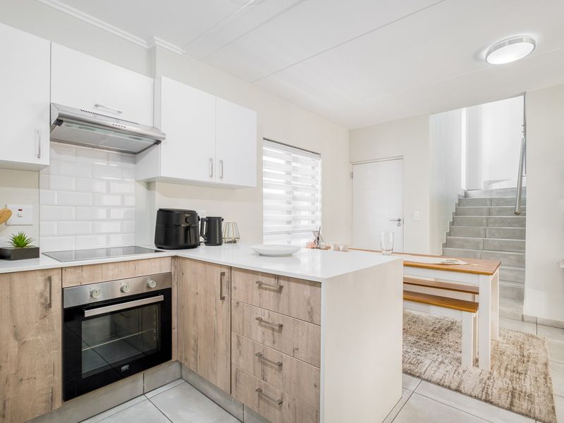 Modern open-plan kitchen featuring light wood-look cabinetry, stone countertops, subway tile backsplash, and integrated appliances, adjacent to a staircase.