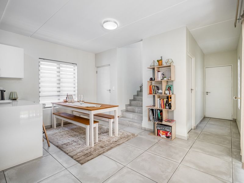 Bright open-plan living and dining area featuring neutral tiled flooring, a modern staircase, and clean white finishes throughout the space.