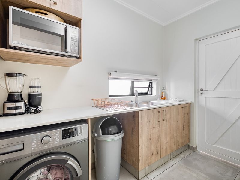 A functional laundry room featuring built-in wood-look cabinetry, a stainless steel sink, integrated microwave space, and direct access to the exterior.