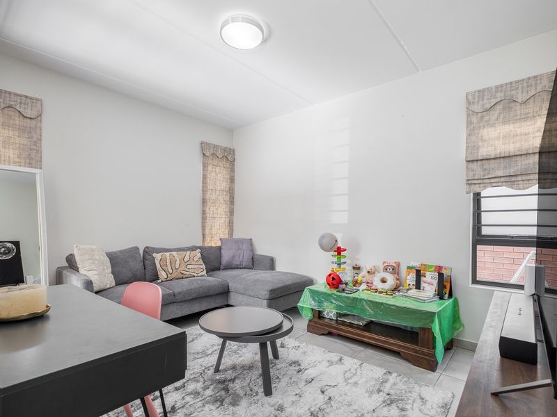 A functional living room featuring tiled flooring, louvered windows, and a central flush mount ceiling light.
