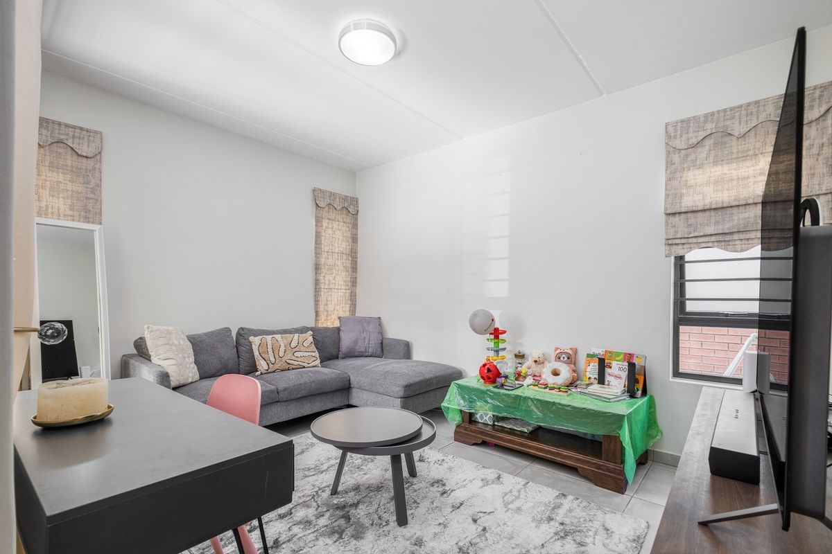 A functional living room featuring tiled flooring, louvered windows, and a central flush mount ceiling light.