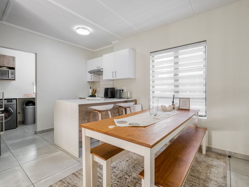 Modern open-plan kitchen and dining area featuring sleek cabinetry, a breakfast counter, and tiled flooring, with an adjacent laundry space.