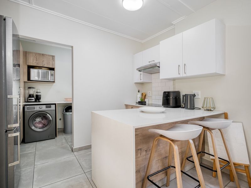 Modern kitchen featuring white cabinetry, stone countertops, a breakfast bar, and a tiled backsplash, with an adjacent scullery area.