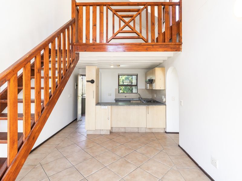 Open plan living area featuring a wooden staircase leading to a mezzanine level, with an integrated kitchen including cabinetry, hob, and extractor fan.