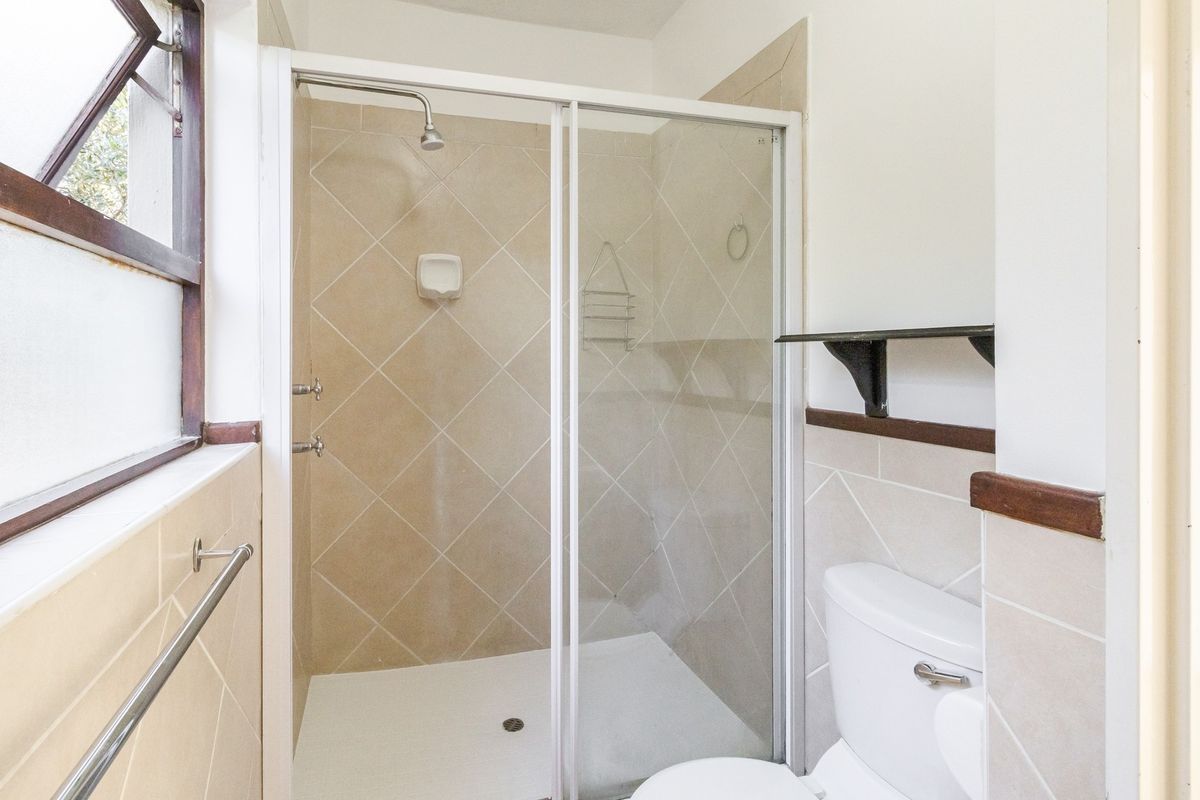 A functional bathroom featuring a tiled shower enclosure with a sliding glass door, a standard toilet, and a window for natural light.