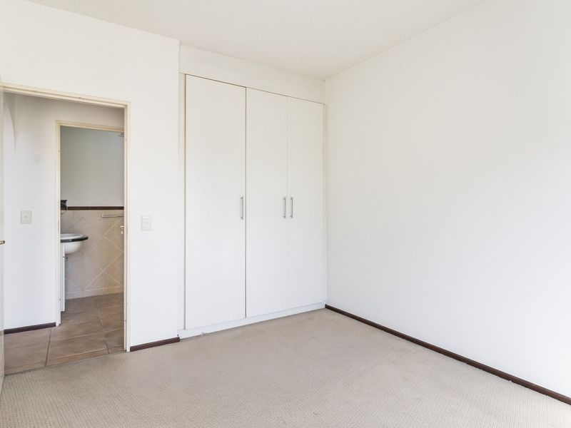 A clean, empty bedroom featuring neutral carpet flooring, built-in cupboards, and direct access to an en-suite bathroom.