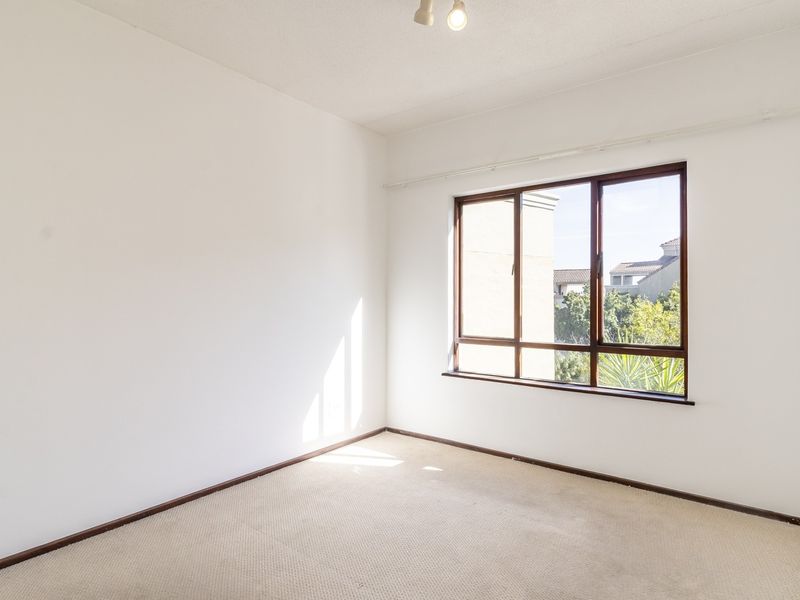 A bright, empty bedroom featuring neutral carpeted flooring, white walls, and large aluminium-framed windows allowing for natural light.