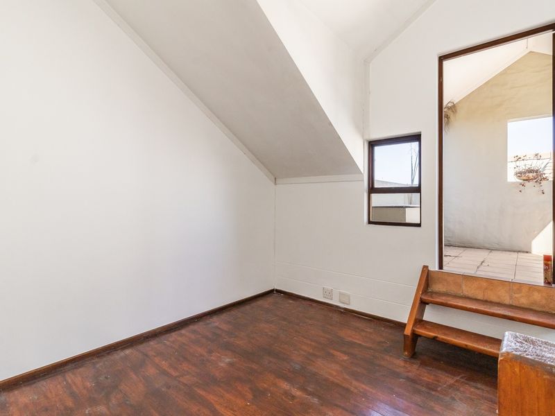 An empty bedroom featuring sloped ceilings, timber flooring, and direct access to an outdoor area via built-in steps.