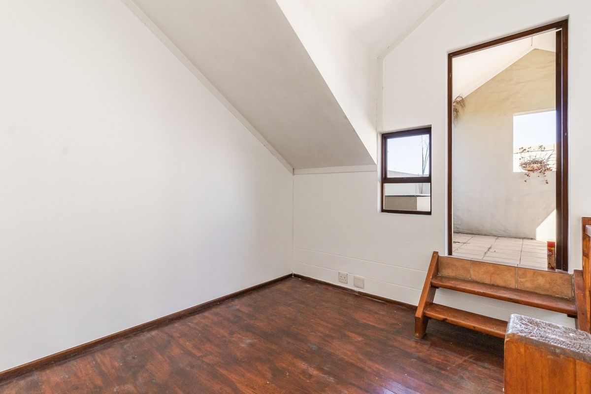 An empty bedroom featuring sloped ceilings, timber flooring, and direct access to an outdoor area via built-in steps.