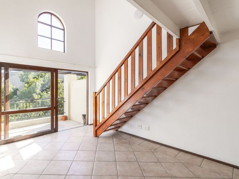 Bright living area featuring a wooden staircase, high ceilings with an arched window, and direct access to a private balcony through sliding glass doors.