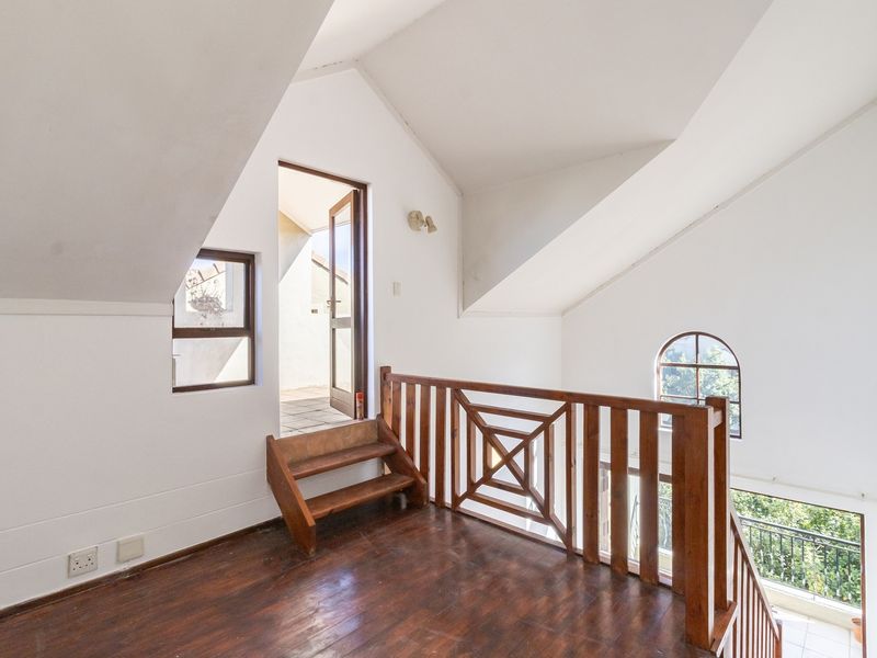 An empty loft-style landing area featuring vaulted ceilings, timber flooring, and a wooden balustrade overlooking the lower level, with access to an outdoor balcony.