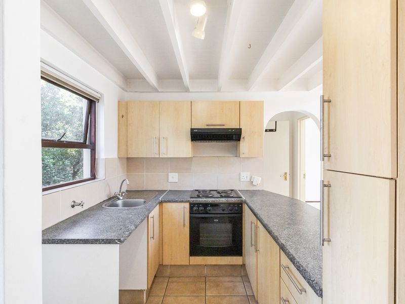 A functional kitchen featuring light wood cabinetry, dark laminate countertops, built-in oven and hob, tiled backsplash, and exposed ceiling beams.