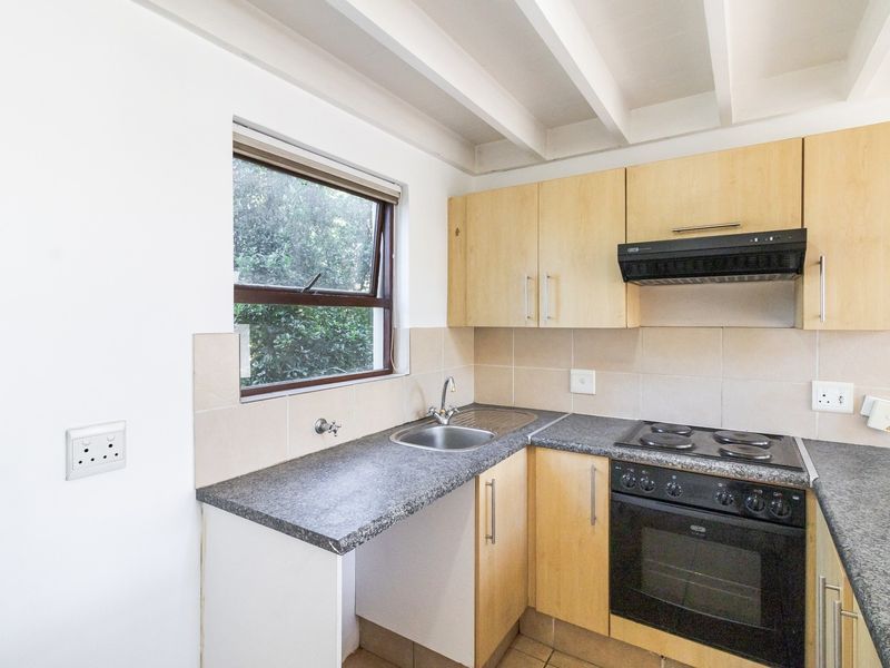 Compact kitchen featuring light wood cabinetry, granite countertops, built-in oven with hob, extractor fan, and tiled backsplash under exposed ceiling beams.