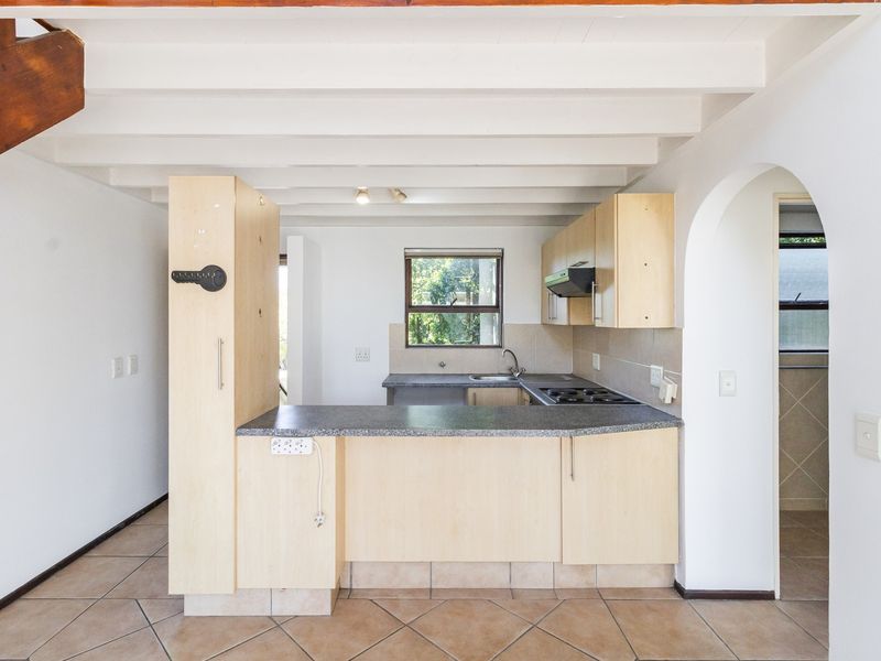 A functional kitchen featuring laminate cabinetry, a built-in hob with extractor, and tiled flooring, set under an exposed beam ceiling with an arched entryway.