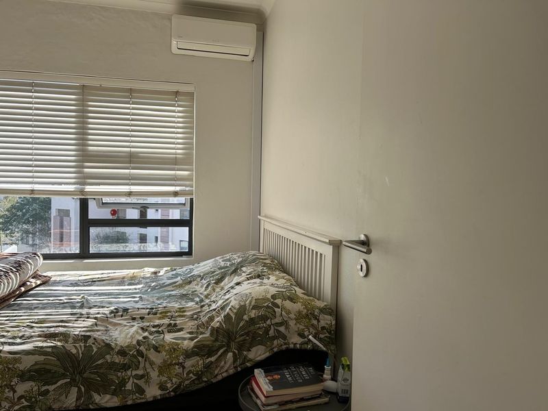 A functional bedroom featuring a wall-mounted split-system air conditioner, venetian blinds, and an aluminium-framed window.