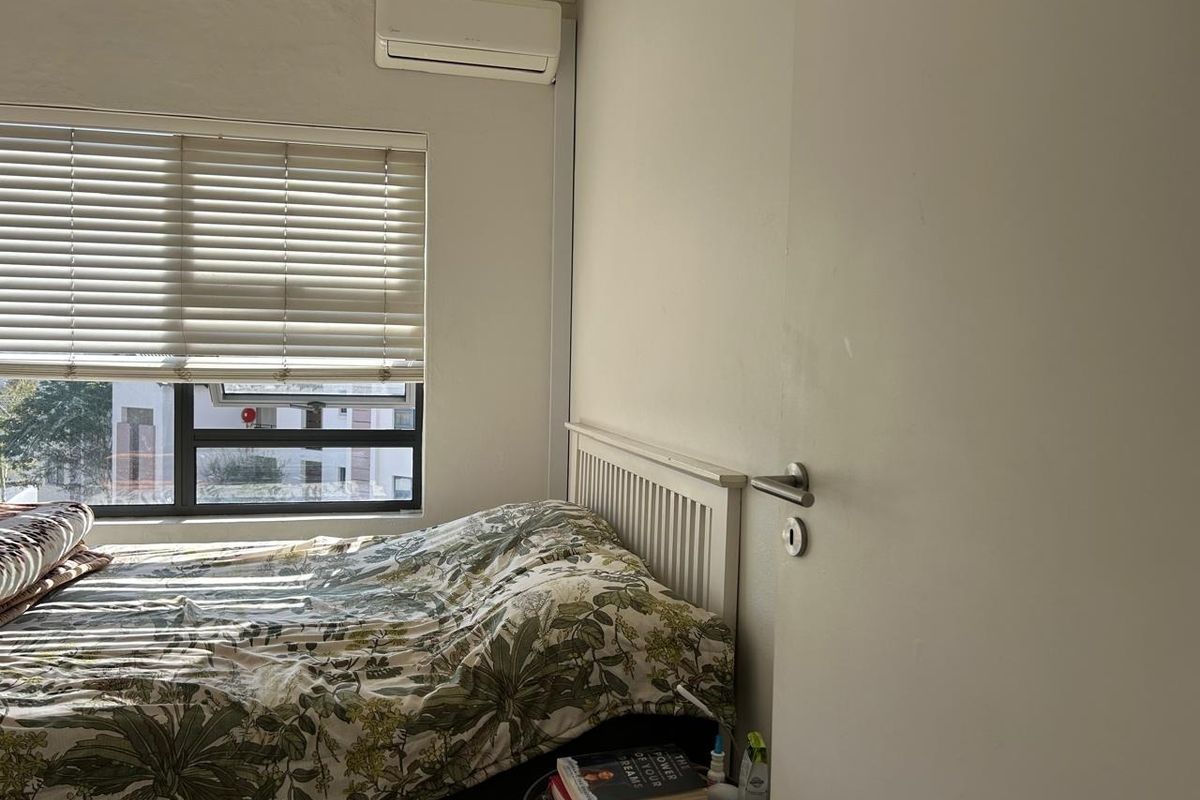 A functional bedroom featuring a wall-mounted split-system air conditioner, venetian blinds, and an aluminium-framed window.